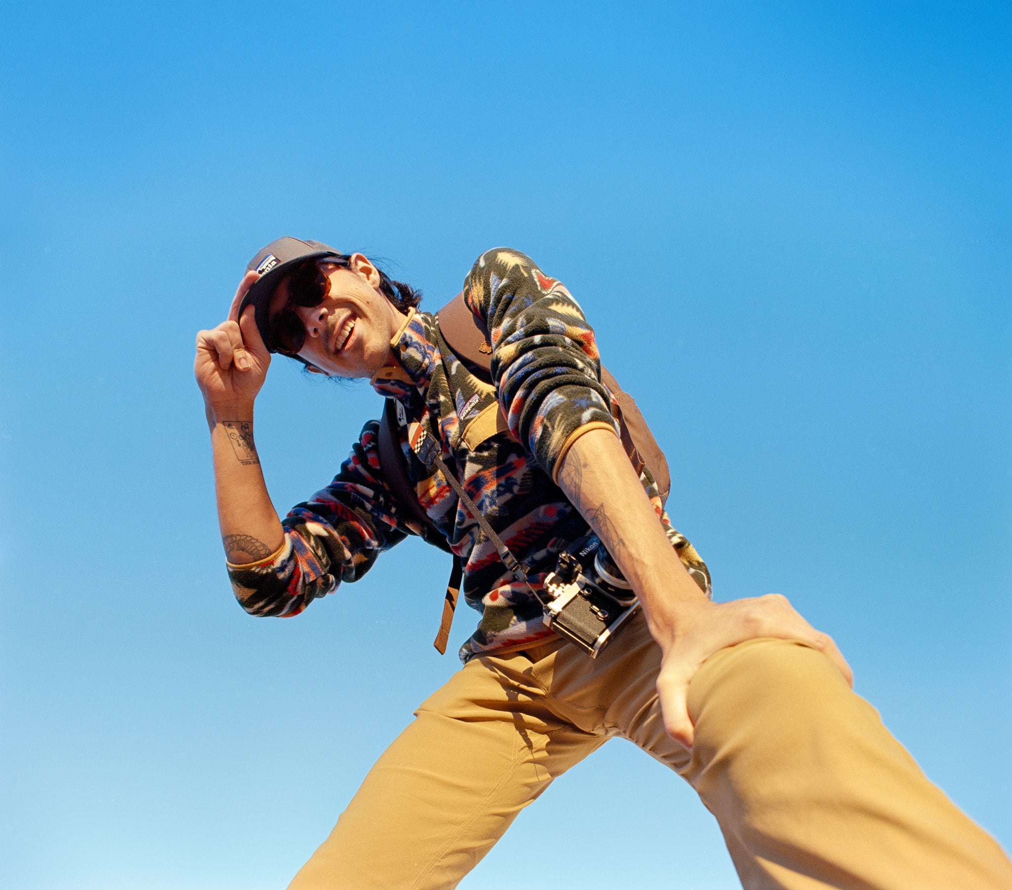 Person wearing a colorful jacket and tan pants against a clear blue sky